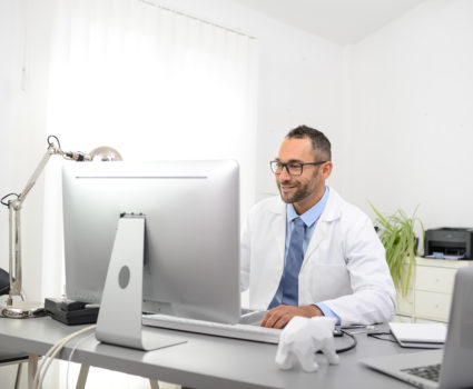 portrait of a handsome man male doctor in medical practice office working on computer